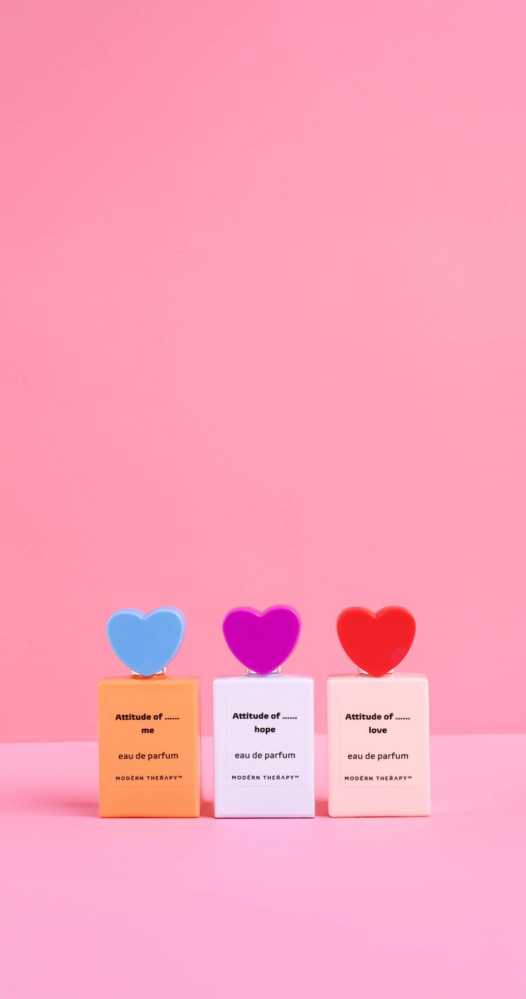 Three small perfume bottles with colorful hearts on a pink background